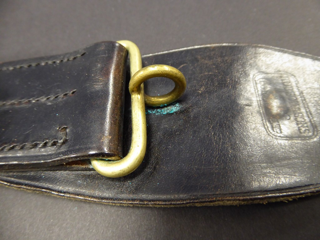 A leather belt with a metal clasp. Under the clasp is a blue powdery substance, which is the result of a chemical reaction between the two materials.