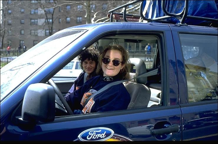 A woman smiles out the window of a blue Ford car.