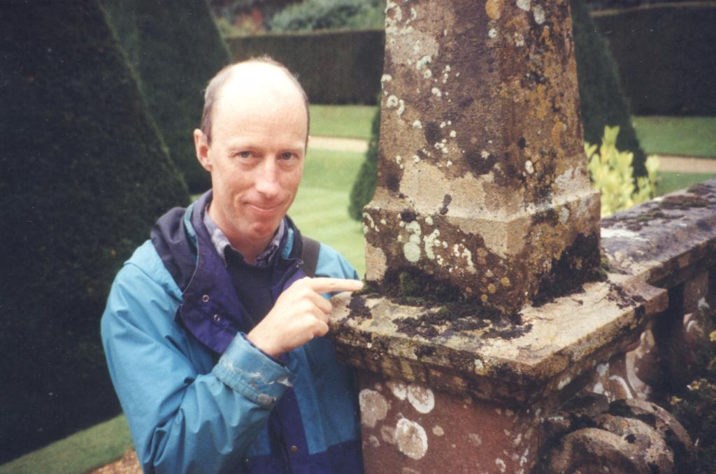 Dr Mike Simms wearing a blue coat pointing at lichen growing on stone