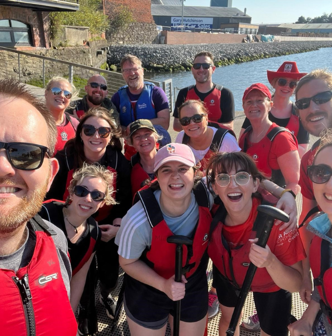A group of men and women in red lifejackets smiling for a picture at the Belfast Lagan
