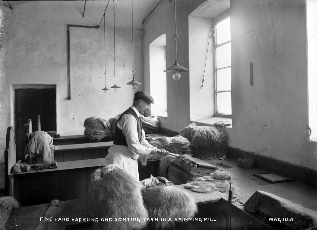 a man hackling flax by hand at a bench by a window
