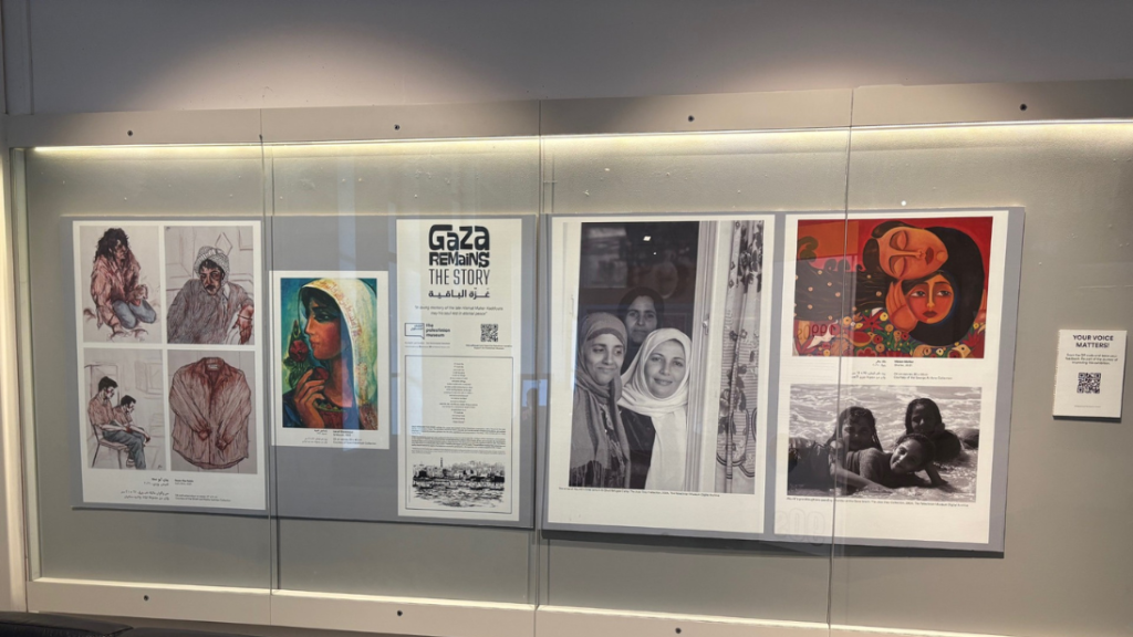 A glass fronted cabinet on a white wall with two down lights displaying panels in an exhibition display